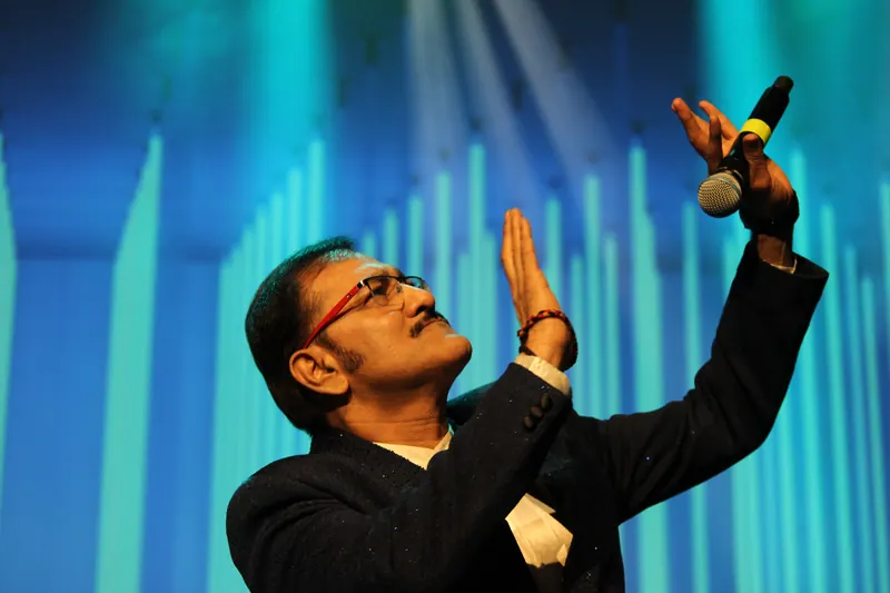 Performer with hands raised, teal stage lighting