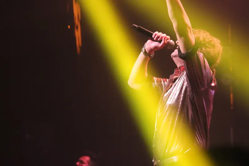 Singer reaching upward through a yellow spotlight